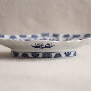 May include: A white ceramic serving dish with a blue and white floral design. The dish has a scalloped edge and a raised base.