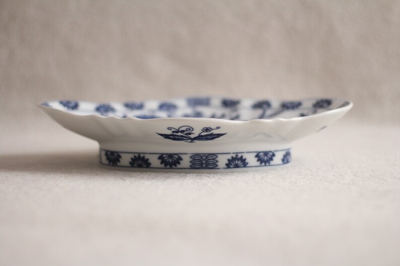 May include: A white ceramic serving dish with a blue and white floral design. The dish has a scalloped edge and a raised base.