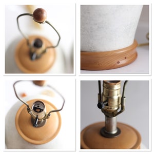 May include: Close-up of a white ceramic lamp base with a wooden base. The lamp has a brass socket and a black switch. The lamp is in the off position.