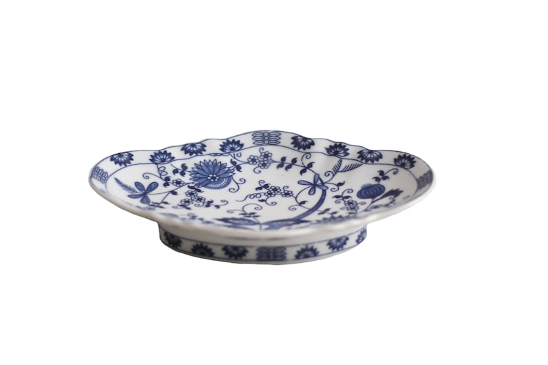 May include: A white ceramic serving dish with a blue floral pattern. The dish has a scalloped edge and a raised base.