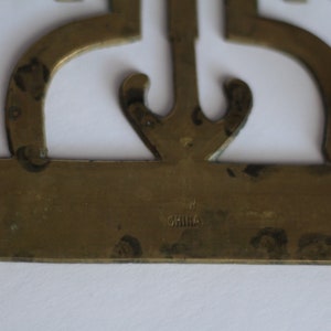Op de afbeelding: Decoratief voorwerp van messing met een ingewikkeld ontwerp en de inscriptie "CHINA" aan de onderkant.