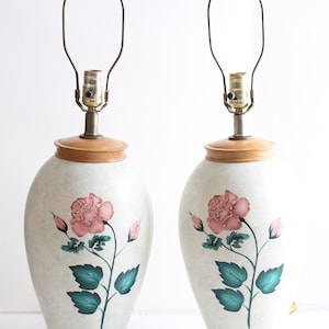 May include: A pair of ceramic table lamps with a white base and a pink rose design. The lamps have a wooden base and a brass lampshade.