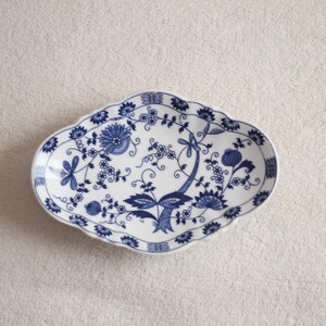 May include: A white oval serving dish with a blue and white floral pattern. The dish has a scalloped edge.