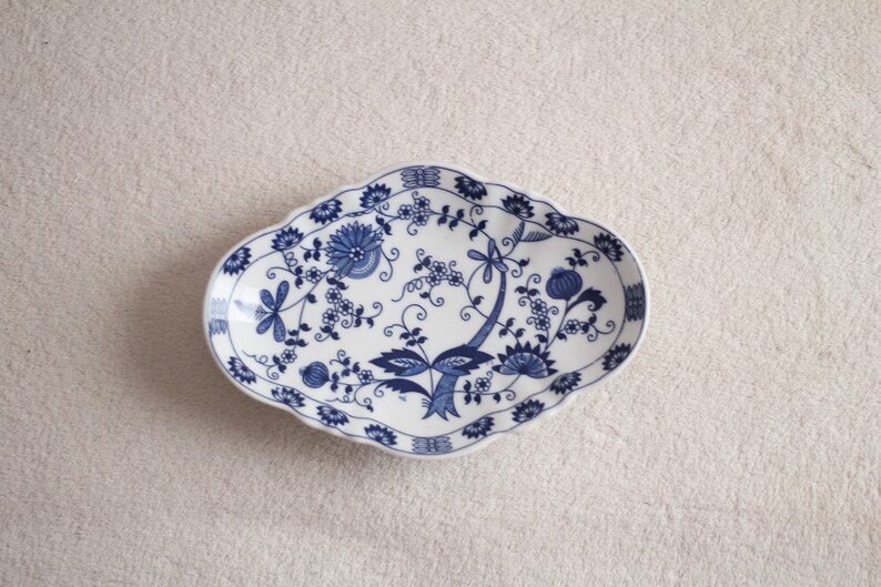 May include: A white oval serving dish with a blue and white floral pattern. The dish has a scalloped edge.