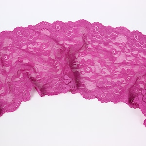 Puede incluir: Primer plano de un ribete de encaje rosa con un patrón floral. El encaje es delicado y tiene un borde festoneado.