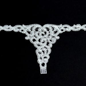 Puede incluir: Borde de encaje blanco con un delicado diseño floral. El borde tiene forma de V y un borde festoneado.