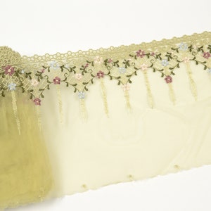 May include: A close-up of a pale green lace trim with a floral design. The trim features small, colorful flowers and green leaves. The lace is delicate and has a scalloped edge.