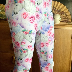 Peut inclure: Legging avec un motif répété de licornes blanches portant des couronnes de fleurs, entourées de roses roses et d'un ciel aquarelle. Le legging est fait d'un tissu doux et extensible.