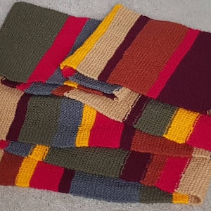 K&ouml;nnte beinhalten: Ein farbenfroher, rechteckiger Schal mit Streifenmuster. Der Schal hat Bl&ouml;cke in verschiedenen Farben, darunter Rot, Gelb, Gr&uuml;n, Beige und Burgunder. Die Enden des Schals haben lange, mehrfarbige Fransen.