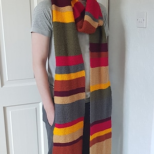 K&ouml;nnte beinhalten: Ein langer, gestreifter Schal in Rot, Gelb, Grau, Braun und Olivgr&uuml;n. Der Schal hat einen Fransenrand und wird um den Hals getragen. Ein markantes Accessoire f&uuml;r Fans einer bekannten Science-Fiction-Serie.