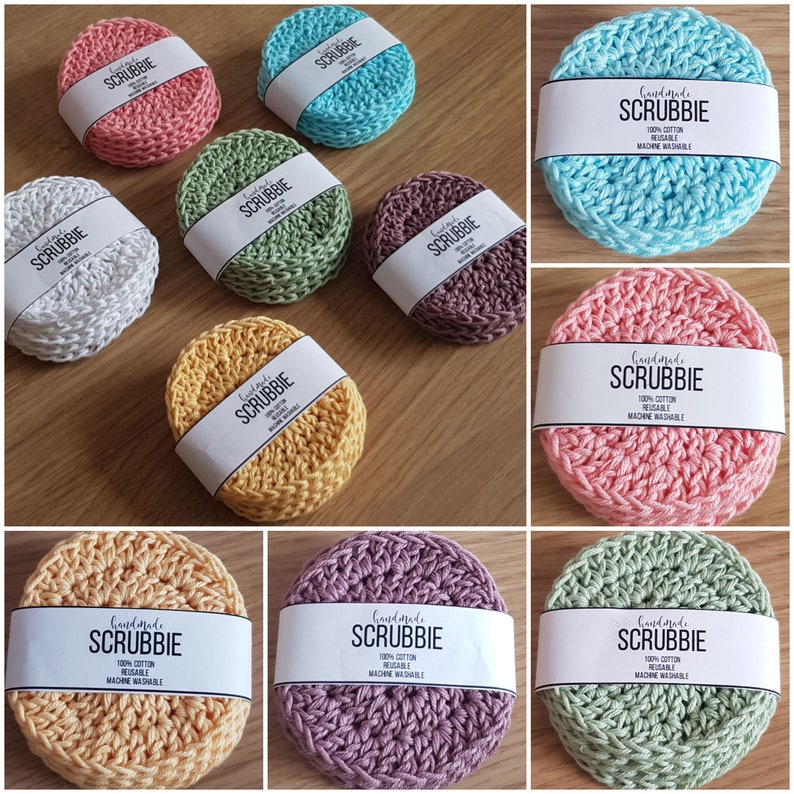 May include: A collection of handmade scrubbies in various colors, including pink, blue, green, and yellow. Each round scrubbie is made of a knitted material and has a white label with the text "SCRUBBIE" and care instructions.