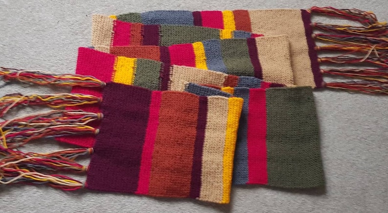 K&ouml;nnte beinhalten: Ein bunter, rechteckiger Schal mit Patchwork-Design. Der Schal hat verschiedene rechteckige Farbbl&ouml;cke in Rot, Gelb, Blau, Gr&uuml;n und Beige. Die Enden des Schals haben lange, mehrfarbige Fransen.