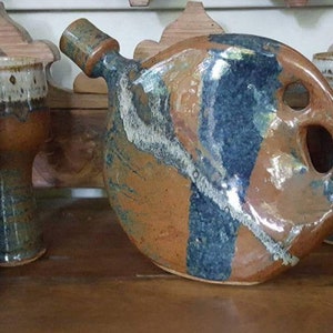 May include: A collection of handmade ceramic drinkware. The set includes four stemmed goblets and a unique, rounded pitcher with a spout and handle. The pieces feature a brown, blue, and white glaze.