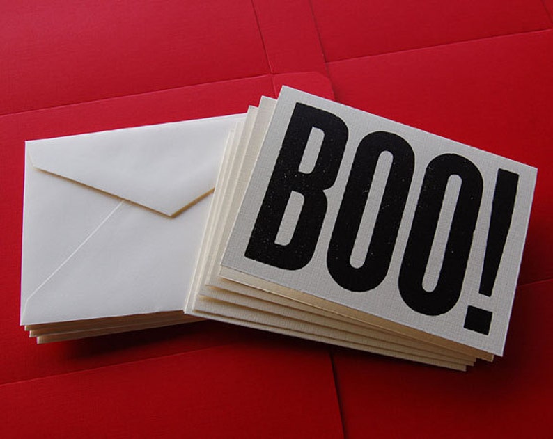 Puede incluir: Una pila de tarjetas blancas con texto negro que dice "BOO!" sobre un fondo rojo.