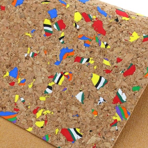 May include: Close-up of a cork material with a speckled pattern. The cork is a light brown color, with colorful flecks of red, blue, yellow, green, and white scattered throughout. The material has a rough texture and is partially covering a tan fabric.