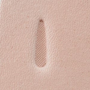 May include: A light beige, textured leather surface featuring a single, elongated, teardrop-shaped indentation. The interior of this recessed shape displays a fine, cross-hatched, diamond-patterned texture, contrasting with the surrounding porous leather.