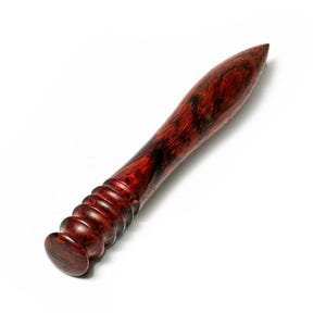 May include: A polished wooden tool with a deep reddish-brown grain and black swirling patterns. The object features a smooth, tapered, pointed end and a handle section characterized by a series of five rounded, stacked circular ridges.