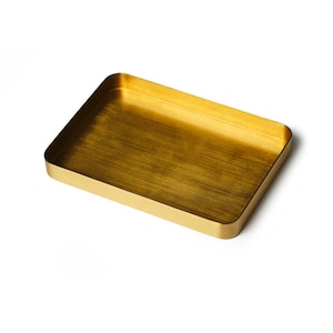 May include: A gold-colored rectangular tray with a brushed finish. The tray is made of metal and has a slightly raised edge.