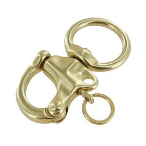 Könnte beinhalten: Ein goldfarbener Schlüsselanhänger aus Metall mit einem großen, runden Ring und einem kleineren, federbelasteten Haken. Der Haken hat eine Drehfunktion und einen kleinen, runden Ring, der daran befestigt ist.