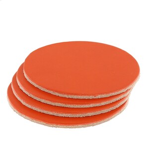 May include: A stack of four orange circular coasters. Each coaster has a smooth, solid orange top and a light tan, textured bottom. The coasters are made of a durable material and are designed to protect surfaces from spills and heat.