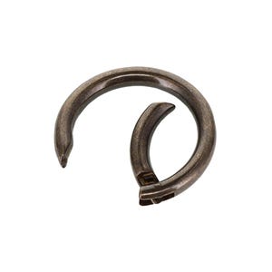 May include: A circular metal spring gate ring with a dark, antiqued bronze finish. The hardware features a hinged opening mechanism that allows the ring to be opened and closed, with a smooth, curved design and a visible joint at the closure point.