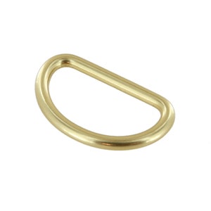 May include: A gold-toned metal D-ring, a type of hardware used for attaching straps, chains, or other accessories.