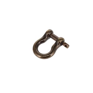 Könnte beinhalten: Ein U-förmiger Metallschäkel mit einer dunklen, verwitterten Bronzeoberfläche. Das Beschlagteil besteht aus einem abgerundeten Körper und einem abnehmbaren, geraden Stift, der in eine Seite geschraubt wird, um eine sichere Schlaufe zu bilden.