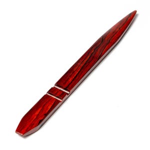 May include: A letter opener crafted from reddish-brown wood. It features a pointed end and a flat, angled base. Two parallel grooves are carved near the handle. The wood grain is visible, enhancing its natural appearance. A stationery item.