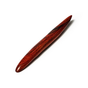 May include: A handcrafted wooden tool with a tapered, pointed end. The tool is a rich reddish-brown color with dark brown grain patterns. The smooth, polished surface suggests it is designed for detailed work or crafting.