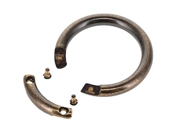 May include: A circular bronze-toned metal handle with a distressed finish, featuring a detachable curved segment and two small threaded screws for assembly. The hardware has a smooth, rounded profile and a weathered, antique-style metallic appearance.