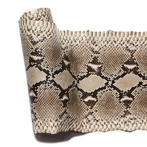May include: A rolled sheet of snakeskin leather featuring a natural scale pattern in shades of beige, tan, and dark brown. The surface displays a repeating diamond-shaped motif with textured, overlapping scales that create a tactile appearance.