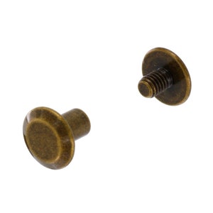 May include: Two antique brass screw-on studs with a round head. The studs are used for attaching fabric or leather to a surface.
