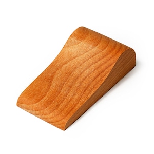 May include: A solid, wooden wedge with a curved top and a slanted base. The wood has a warm, reddish-brown hue and visible grain patterns. The object is likely a decorative or functional item, possibly a display stand or a small ramp.