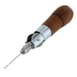 May include: A sewing awl featuring a dark brown wooden handle, a silver metal body, and a sharp needle. The metal component is engraved with the text C.S. OSBORNE & CO. U.S.A. and contains a spool of black thread visible within the frame of the tool.