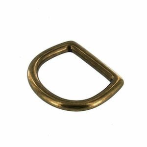 May include: A gold-toned metal D-ring, a type of hardware used for attaching straps, belts, or other accessories.