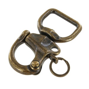 May include: Antique brass swivel trigger snap hook with a round key ring. The hook has a D-ring shape and a spring-loaded trigger.