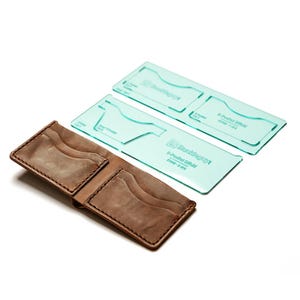 May include: Open brown leather wallet with multiple card slots, next to three transparent green acrylic templates. The templates have text and curved shapes for crafting. The wallet is open, showcasing its interior design.