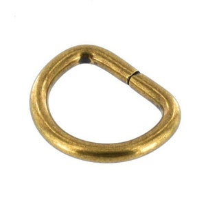 May include: A gold-toned metal D-ring, a type of hardware used for attaching straps, chains, or other accessories.
