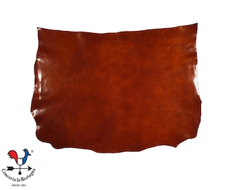 Puede incluir: Una gran pieza rectangular de cuero marrón con un acabado brillante. El cuero tiene un borde natural e irregular y está sobre un fondo blanco. Un logotipo es visible en la esquina inferior izquierda.
