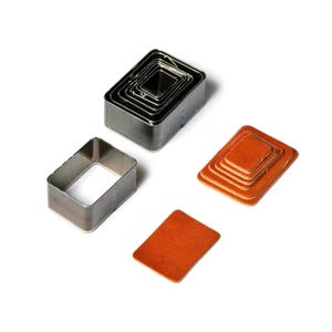 May include: A collection of rectangular metal craft dies and cut leather pieces in various sizes. The dies are stacked, showing a nested design. The leather pieces are in shades of orange and brown, with a smooth texture.