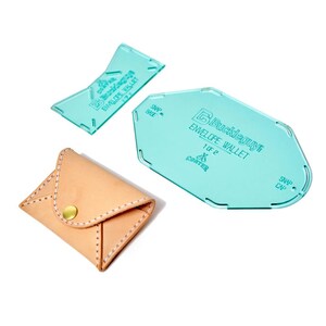 May include: A tan leather envelope wallet with a gold snap closure and white stitching, alongside two teal acrylic templates. The templates are marked with text, including "Envelope Wallet". The wallet is approximately 8 cm wide.
