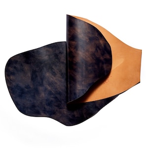 May include: Two pieces of leather, one dark blue and one light brown, are folded and arranged in a wave-like pattern. The leather has a mottled, marbled appearance.