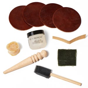 May include: A collection of leather crafting tools and materials, including four brown leather circles, a jar of Tokonole burnishing gum, a wooden burnishing tool, a sponge applicator, and a small piece of green fabric.