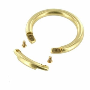 May include: A gold-colored, semi-circular handle with two detached segments and two small screws. The handle is made of a shiny, metallic material and is designed to be attached to a larger object. The pieces are set against a white background.
