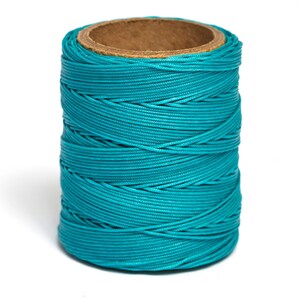 May include: A spool of teal blue waxed thread. The thread is wound tightly around a cardboard spool.