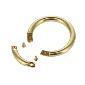 Puede incluir: Un tirador de anillo circular de latón que incluye un segmento de montaje curvo desmontable y dos pequeños tornillos roscados. El herraje presenta un acabado metálico pulido y liso con puntos de fijación visibles para su instalación.