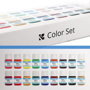 Puede incluir: Una caja blanca con la etiqueta "Color Set" con una variedad de pequeños frascos de pintura en varios colores. Los frascos están dispuestos en filas, con una gama de tonos que incluyen rojo, amarillo, azul y verde. La caja tiene un logotipo en el lateral.