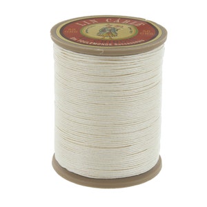 May include: A spool of white linen thread, labeled "Lin Câblé" with a 50 gram weight. The label also features a vintage illustration of a woman in a dress.