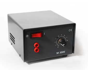 May include: A gray electrical device with a black front panel. The panel features a red on/off switch, a rotary dial with numbers, and two red connectors. The text "M 3000" is printed on the front.