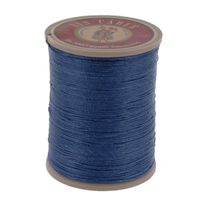 May include: A spool of dark blue thread with a tan label. The label reads "LIN CABLE" and "50 GRS". The thread is tightly wound around the spool, creating a textured surface. The product is likely used for sewing or crafting.